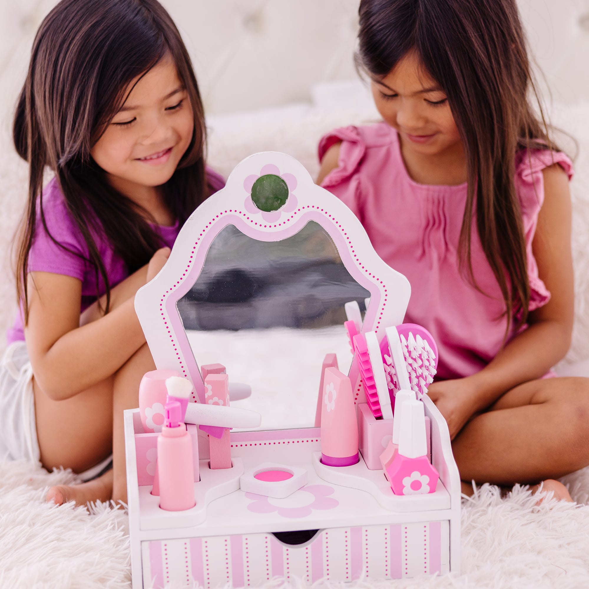 Two children playing with a pink toy vanity set on a white surface.