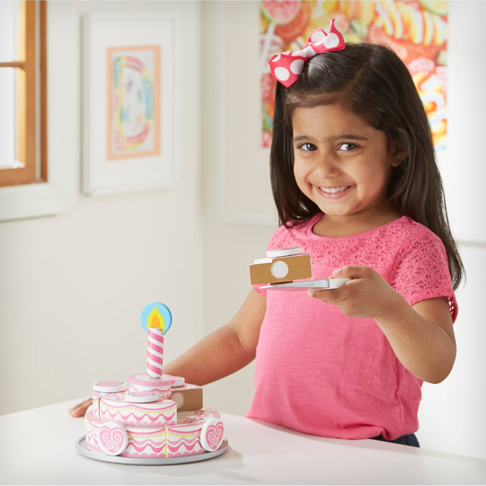 Young girl in a pink shirt with a birthday cake and candle in a room.