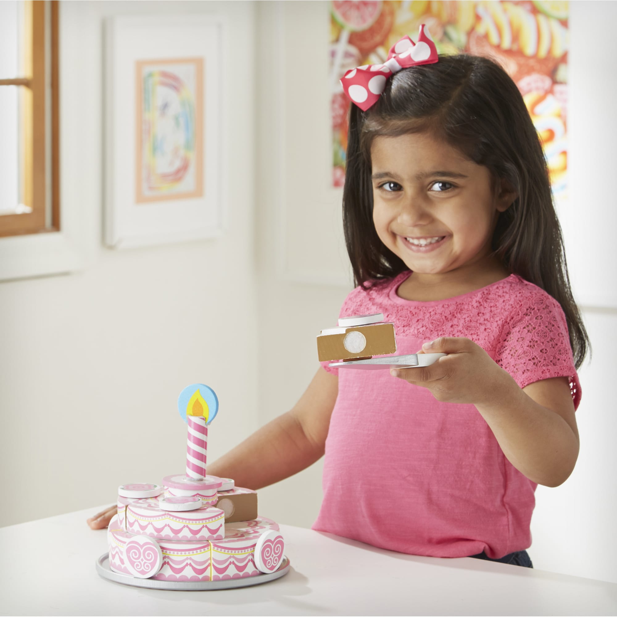 Young girl in a pink shirt with a birthday cake and candle in a room.