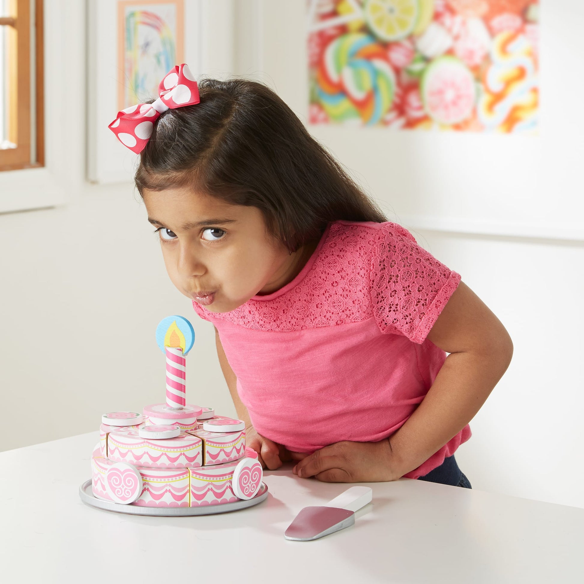 Young girl with a pink bow in her hair, leaning over a small birthday cake with a candle.