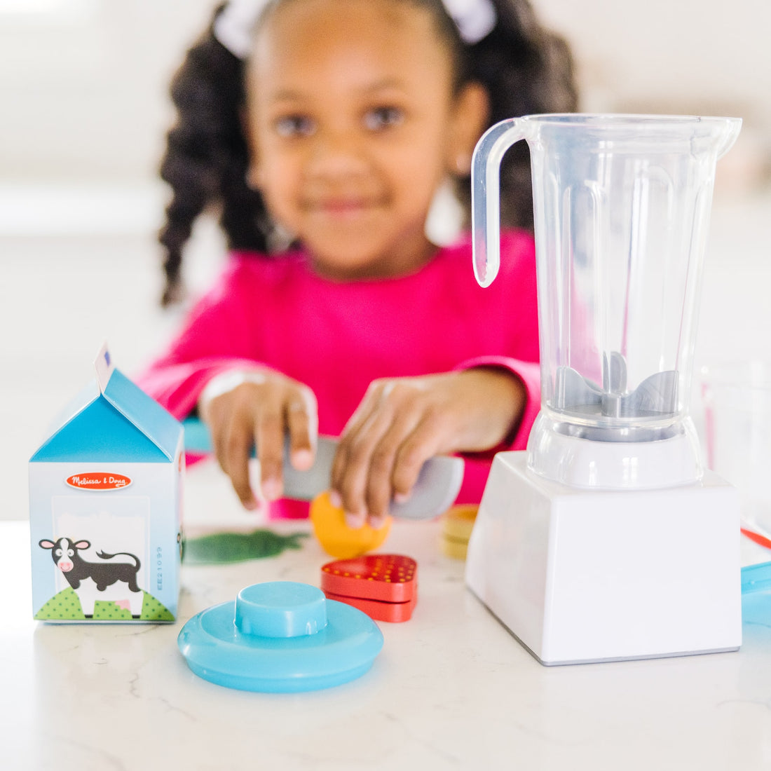 Child playing with toy blender and food items on a table