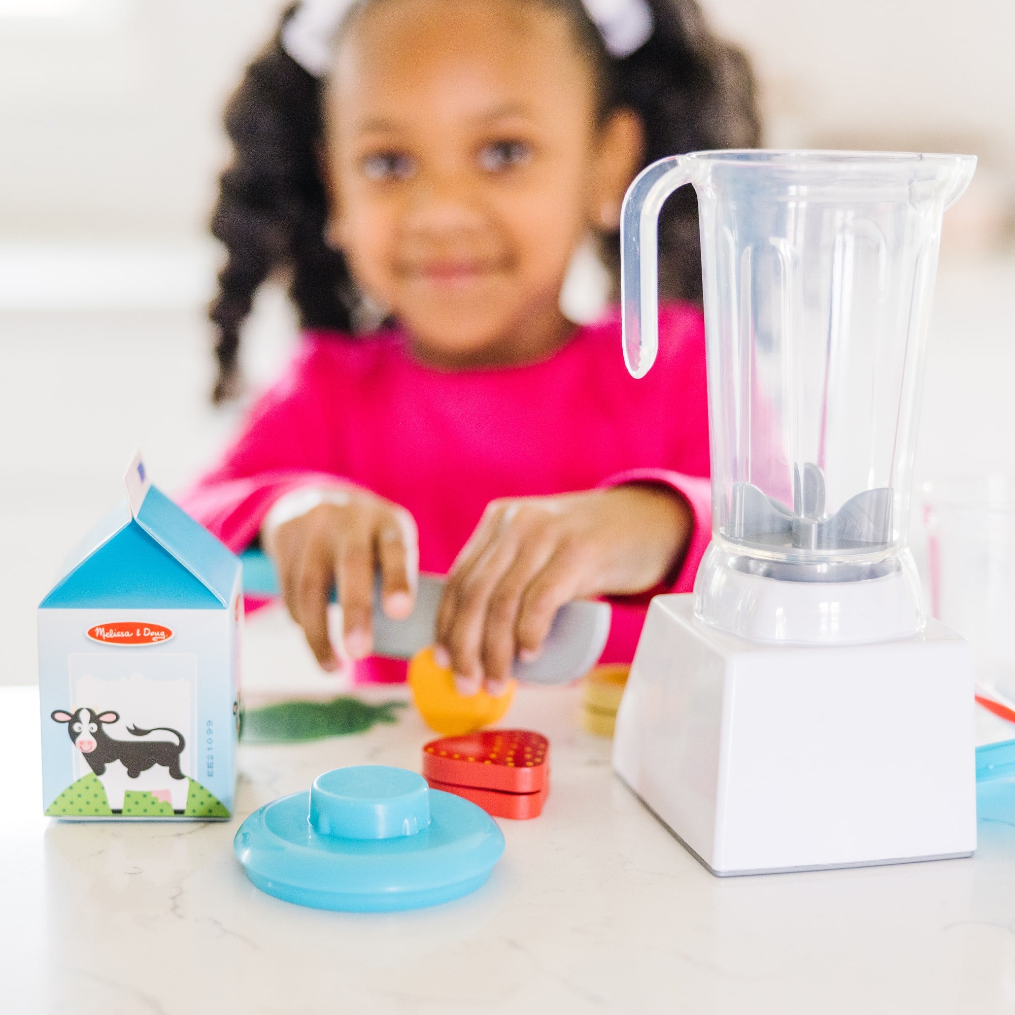 Child playing with toy blender and food items on a table