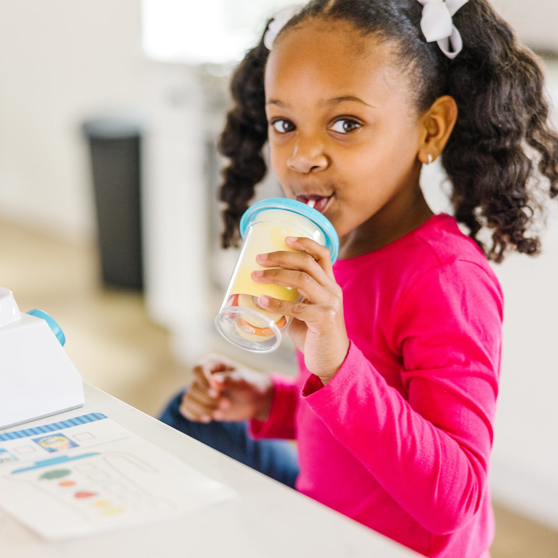 Child holding a yogurt container with a spoon, sitting at a table.