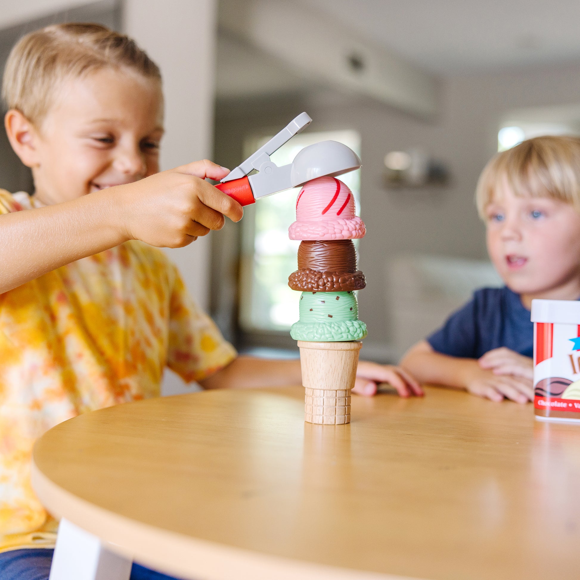 Two children playing with a toy ice cream cone set on a wooden table.