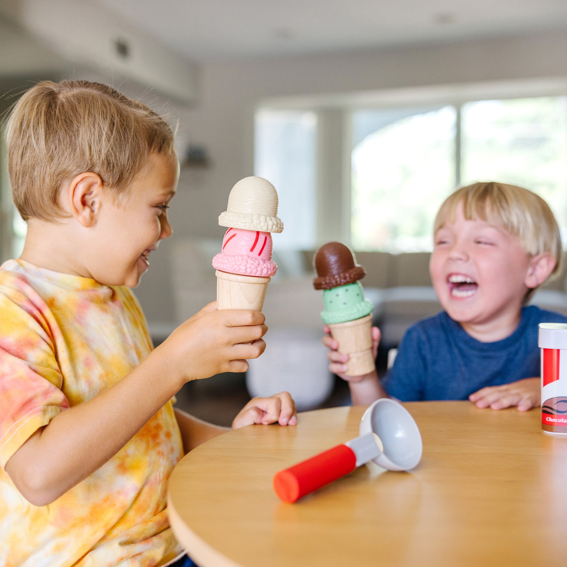 Two children playing with toy ice cream cones at a table.