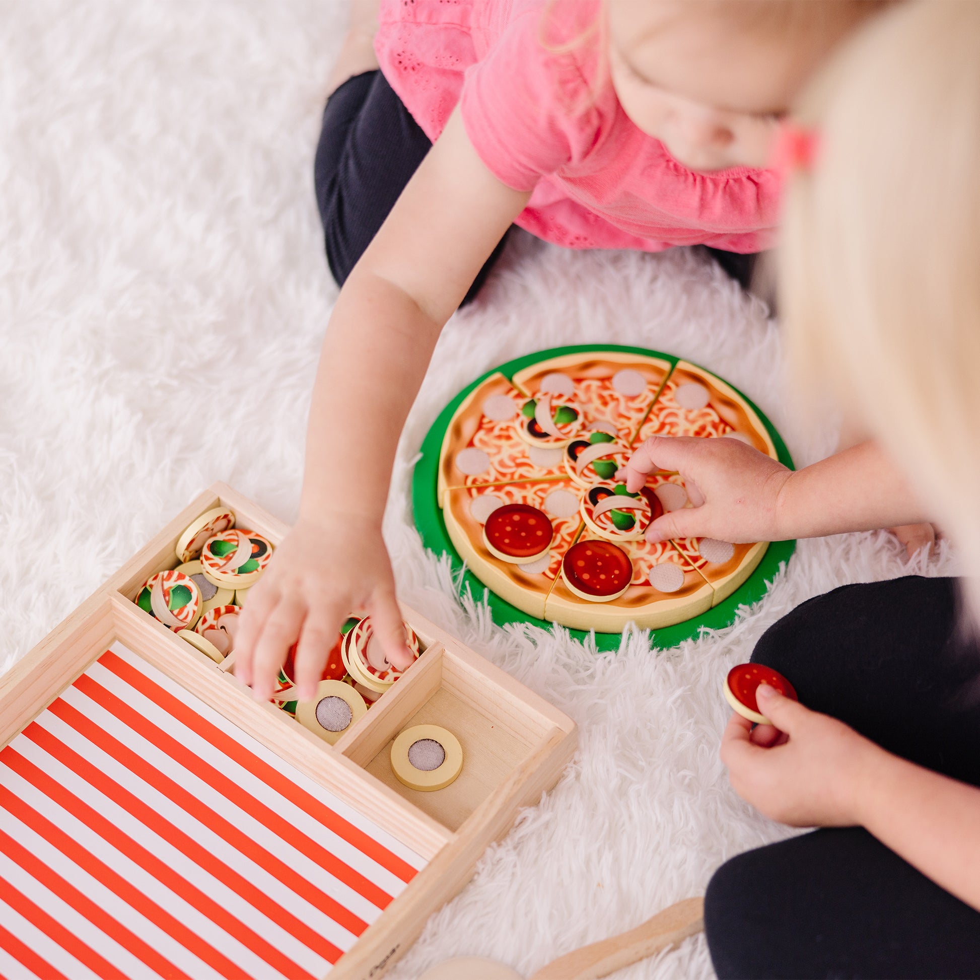 Children playing with a toy pizza and wooden box on a white surface