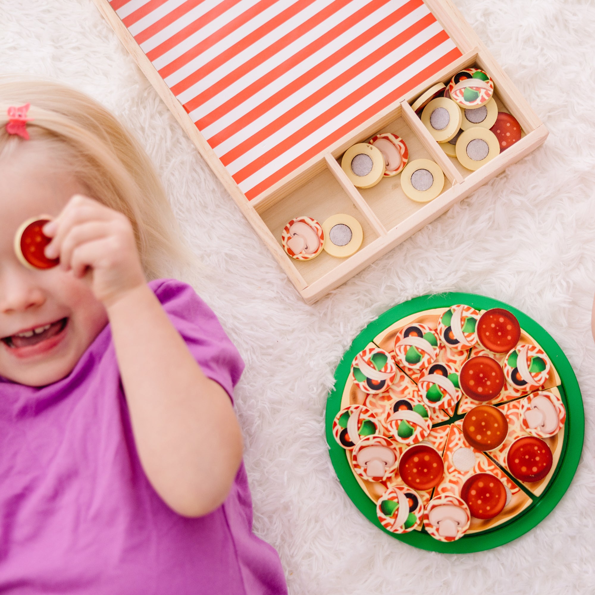 Child playing with a toy pizza and magnet set on a light surface