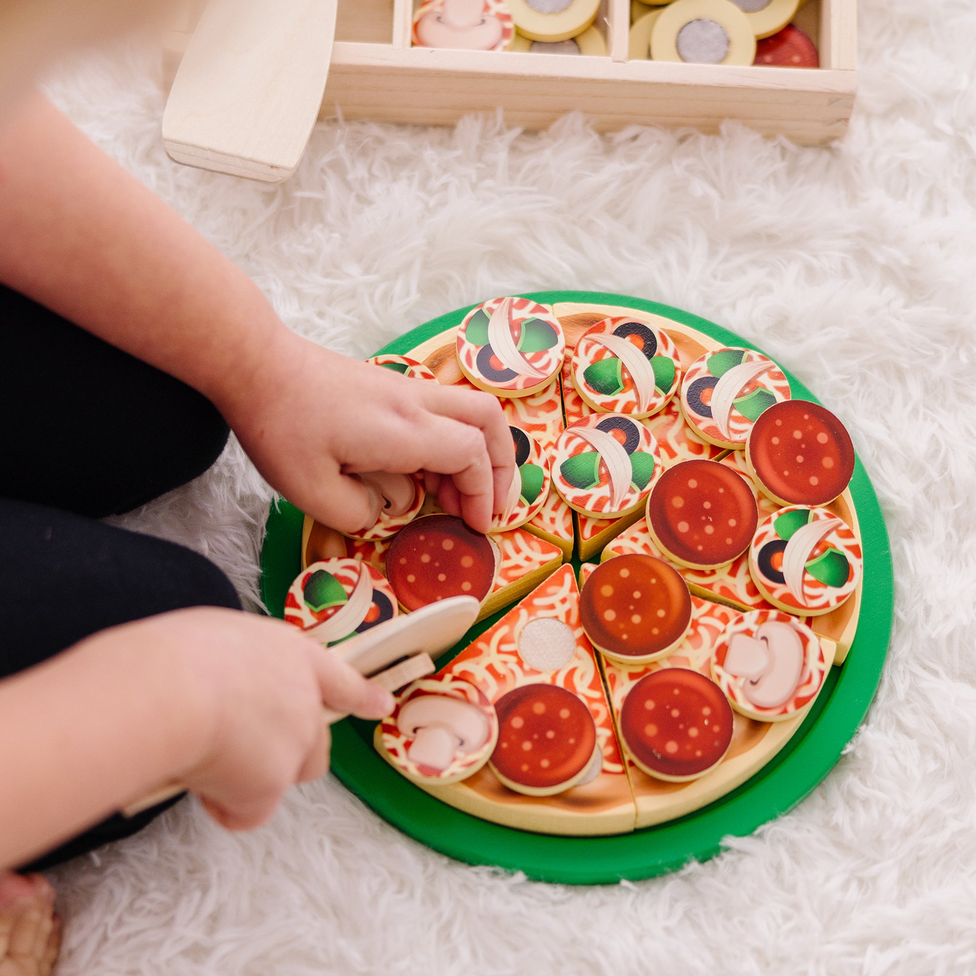 Child playing with a toy pizza set on a fluffy white surface