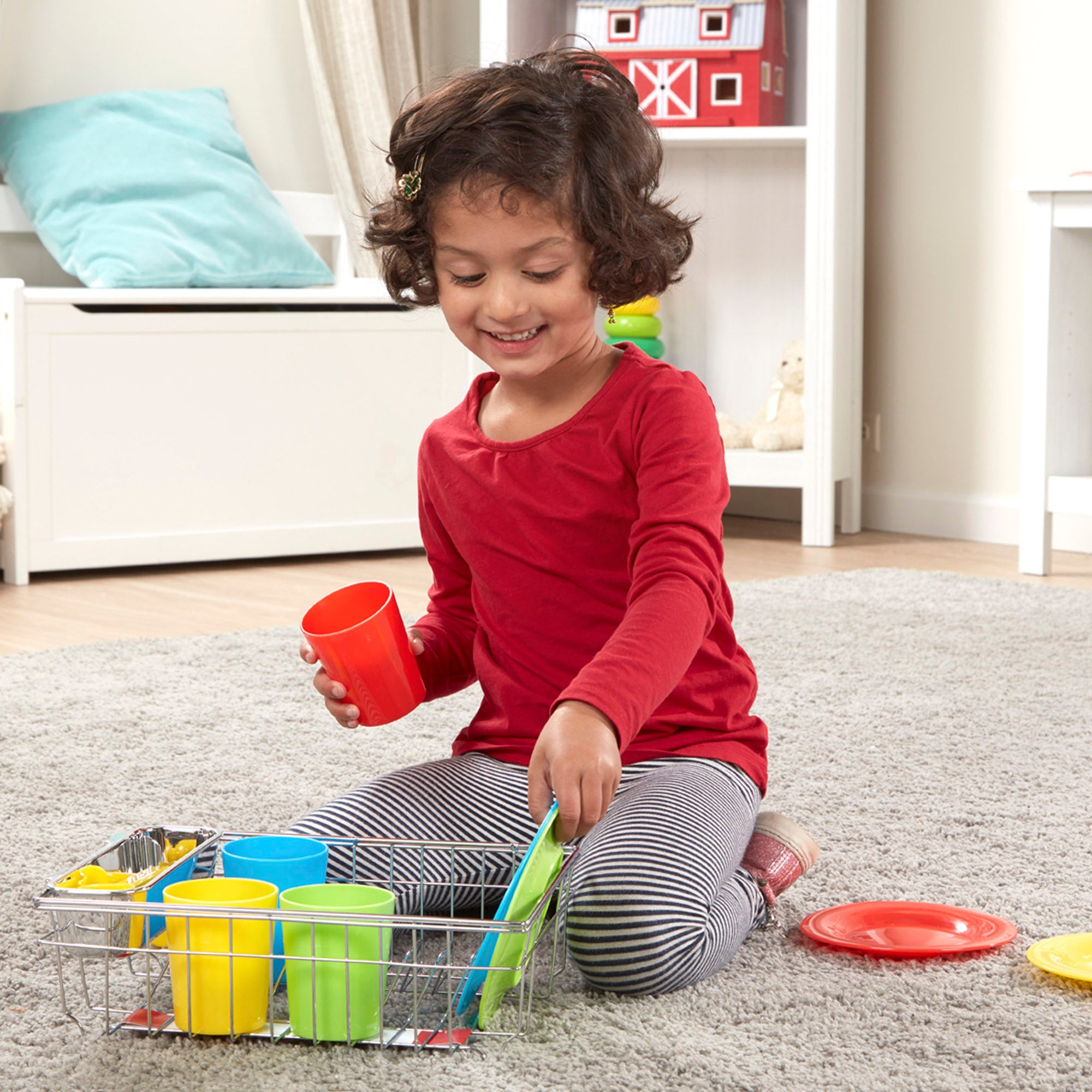 Child playing with colorful cups and a toy kitchen set on a carpeted floor.