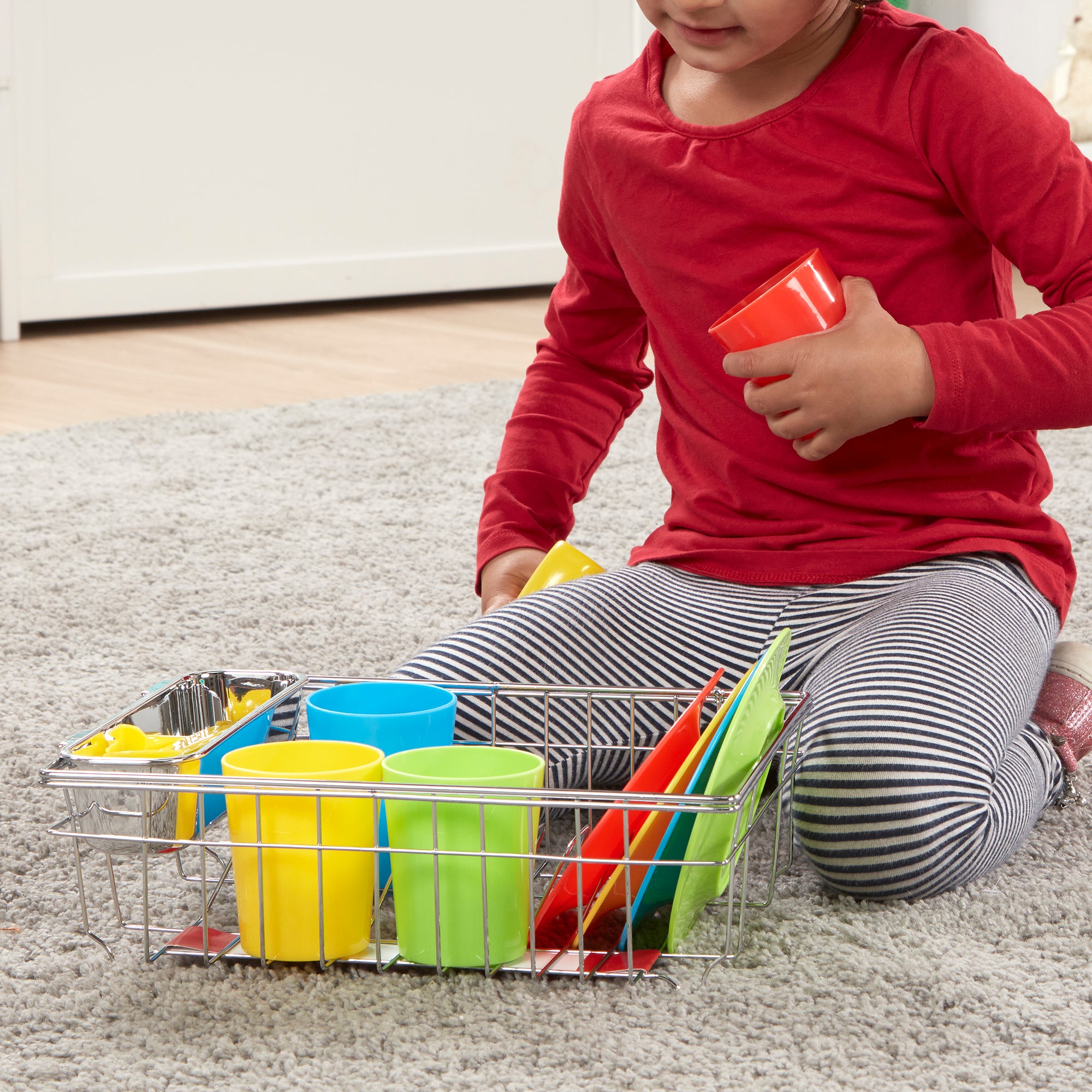 Child playing with colorful cups and a metal basket on a carpeted floor.
