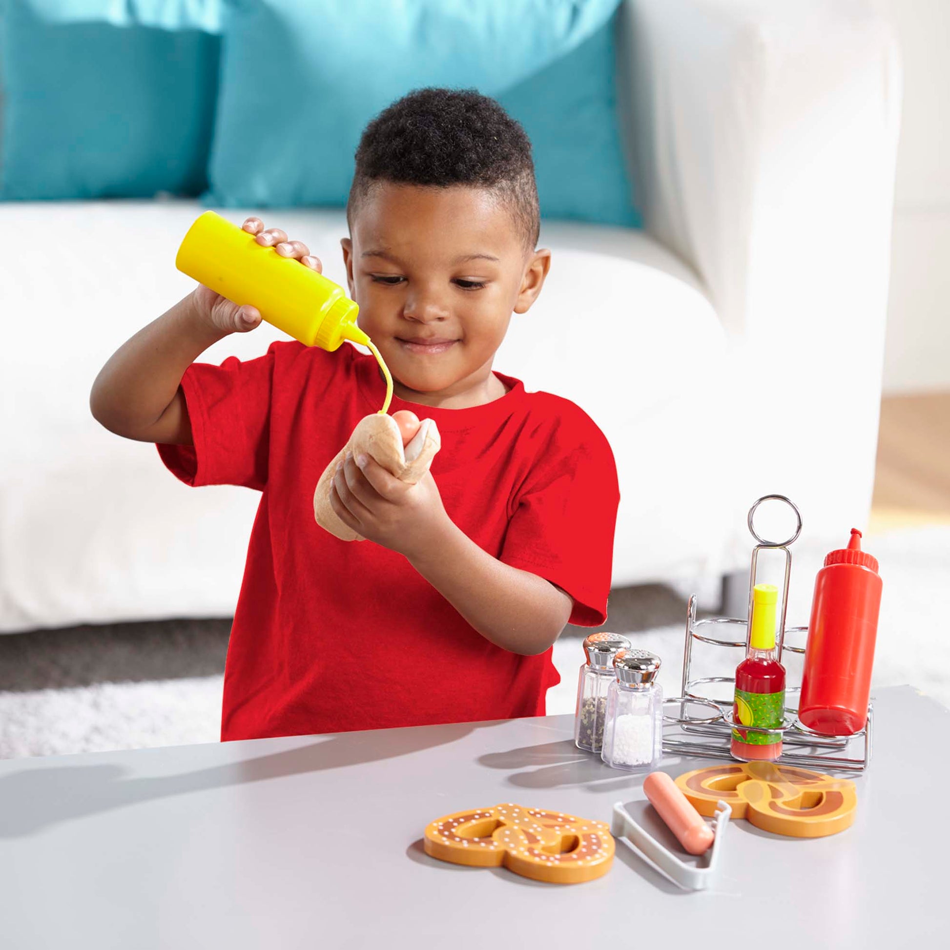 Child playing with toy condiment bottles and food items on a table.