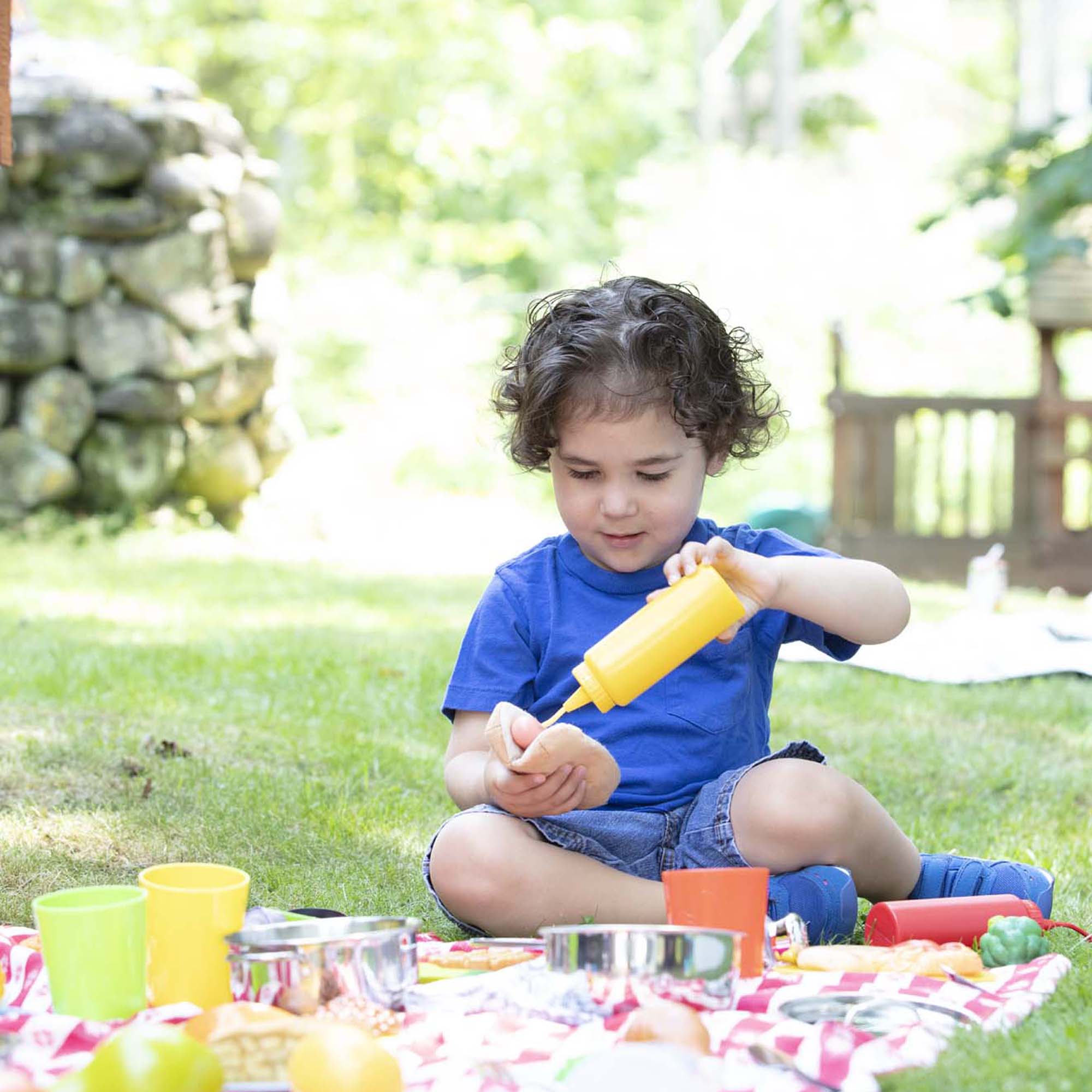 Child playing with toy kitchen set outdoors on a grassy area