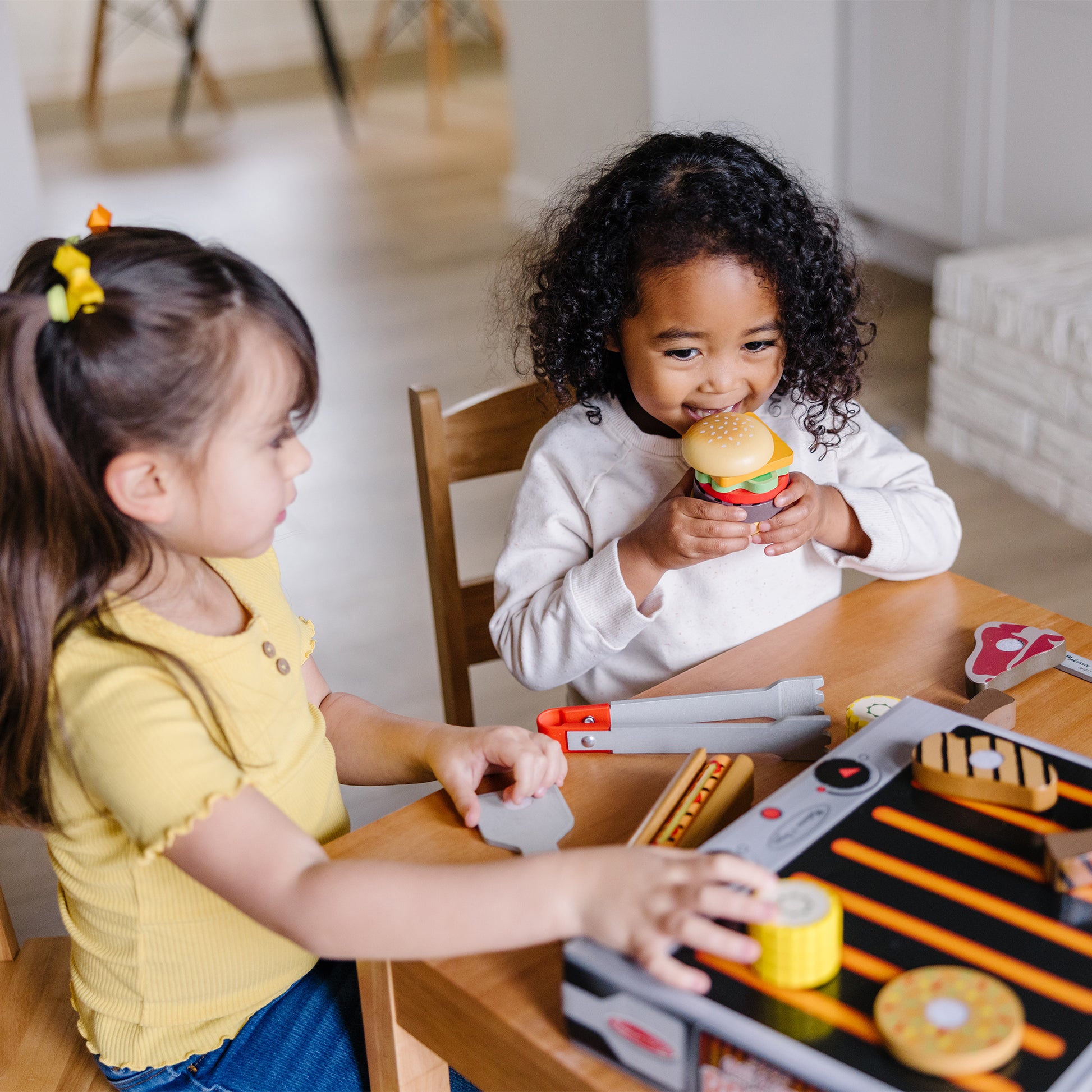 Two children playing with toy kitchen sets at a table.