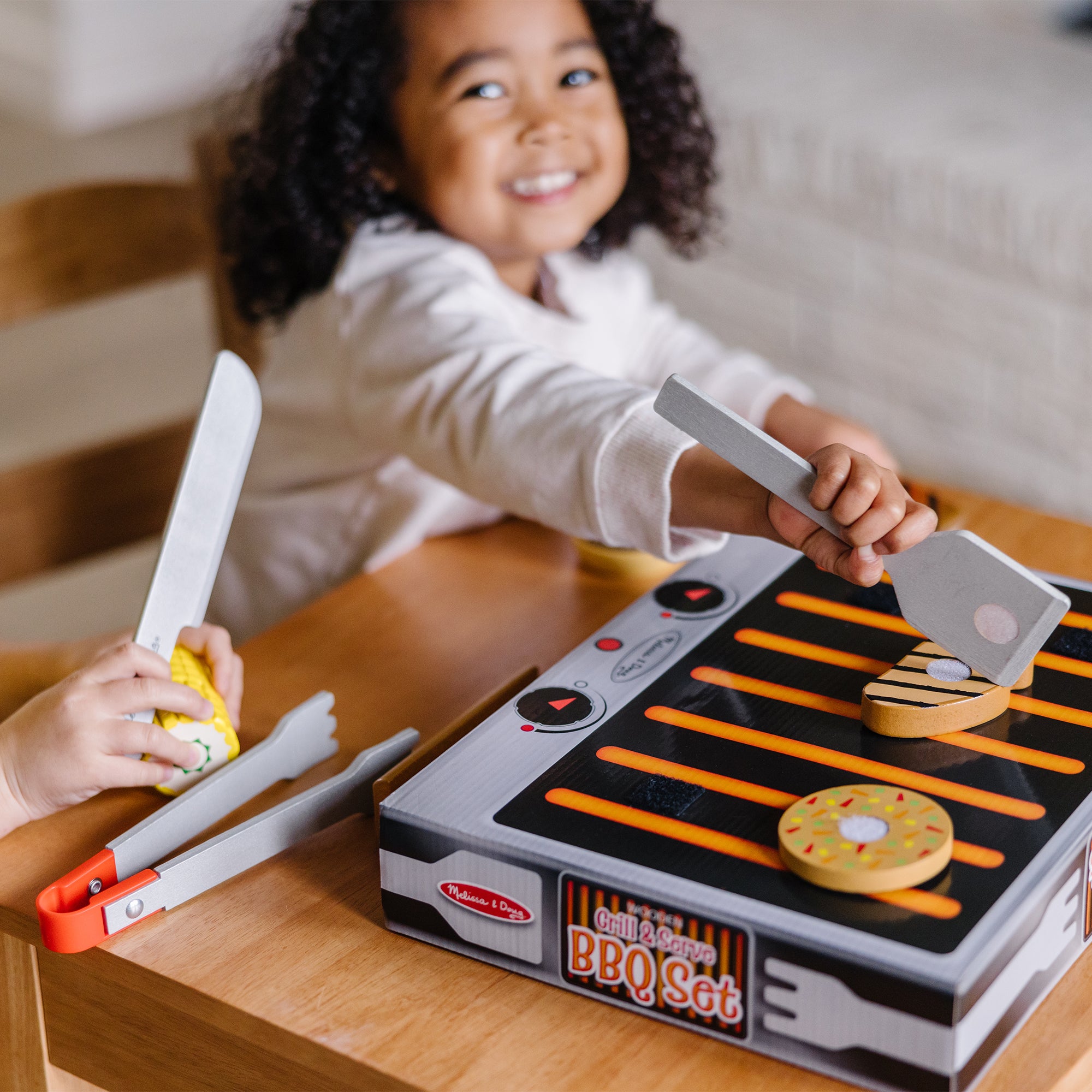 Child playing with a toy BBQ set on a wooden table