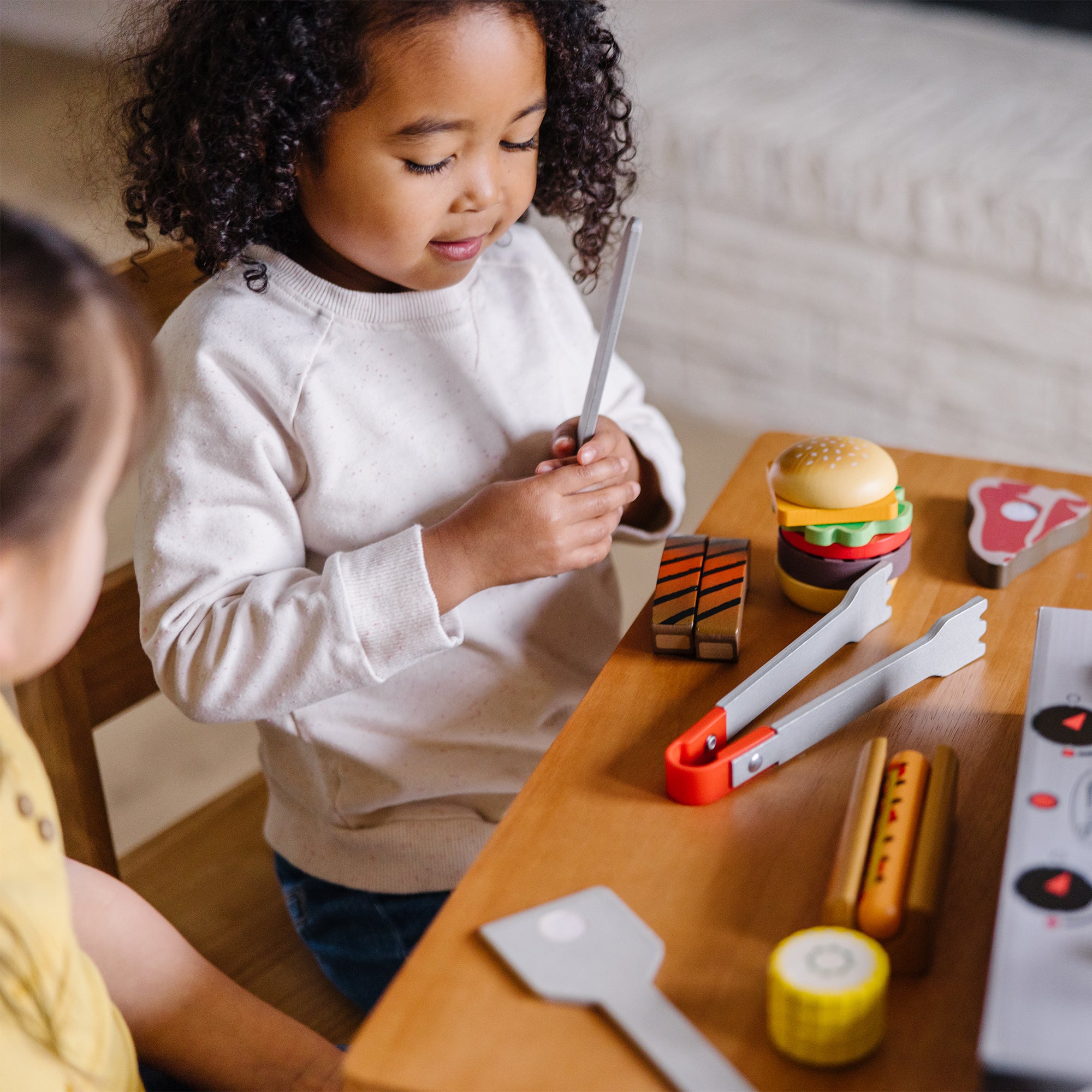 Two children playing with toy kitchen items on a wooden table.