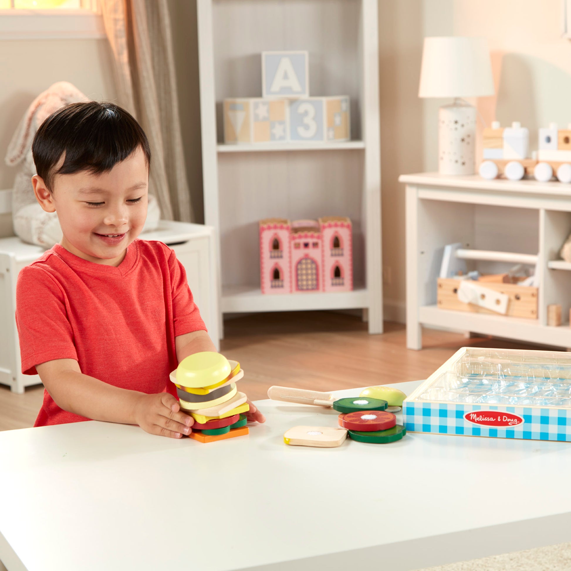Child playing with toy hamburger set in a room with shelves and toys.
