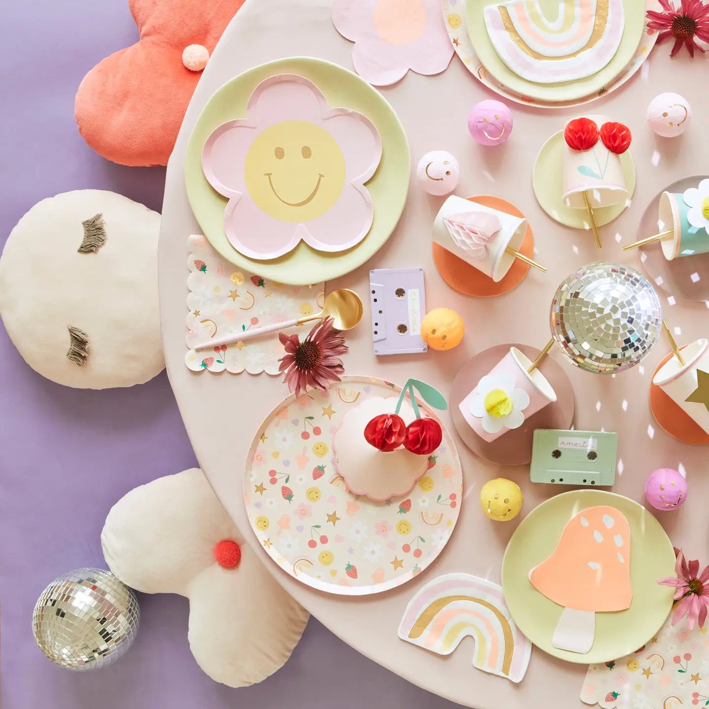 Colorful children's party supplies including plates, cups, and decorations on a pink surface.