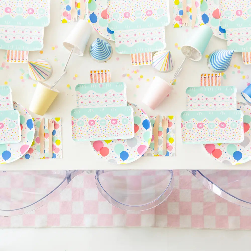 Colorful party supplies including plates, cups, and napkins on a checkered tablecloth.