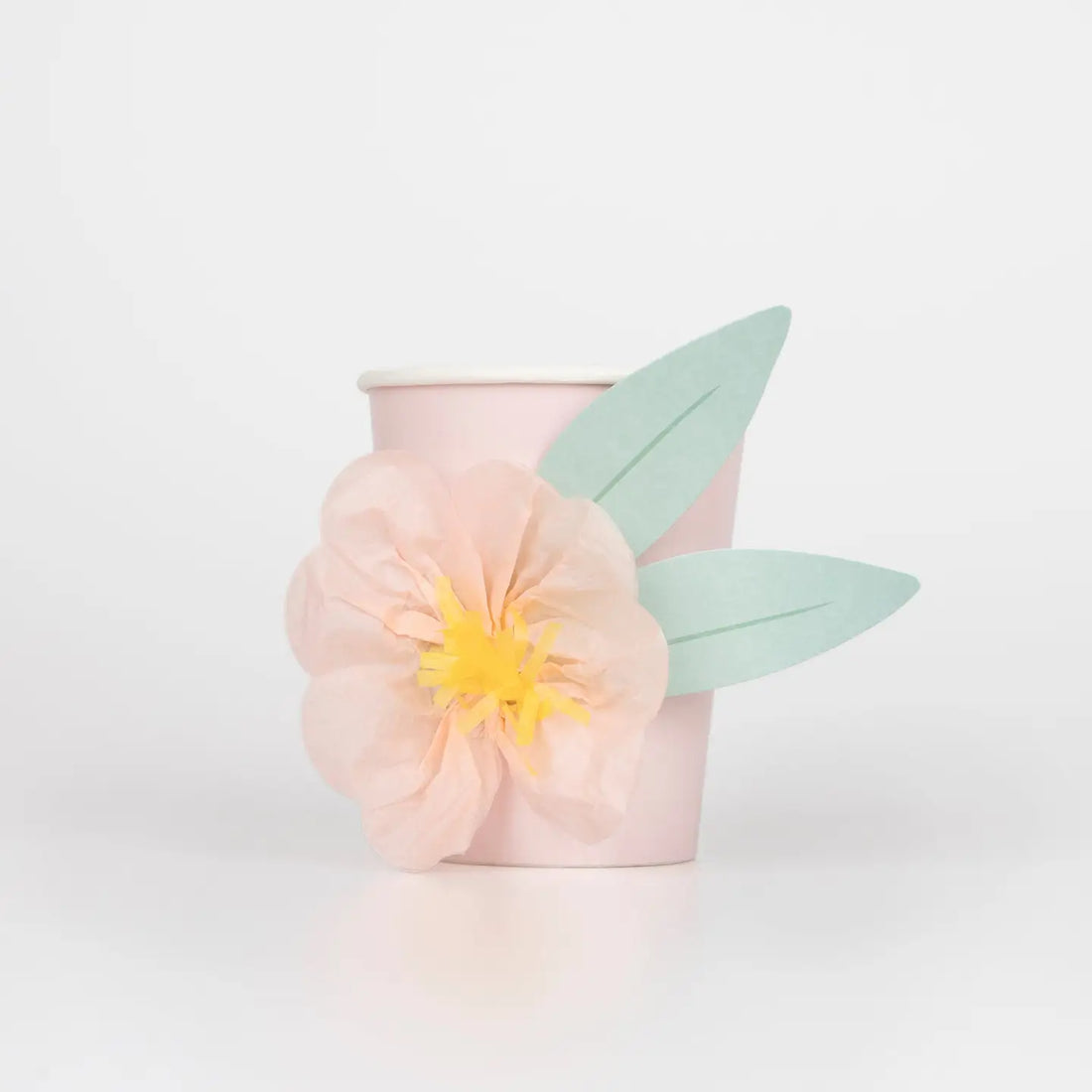 Pink cup with a yellow flower and green leaf on a light gray background