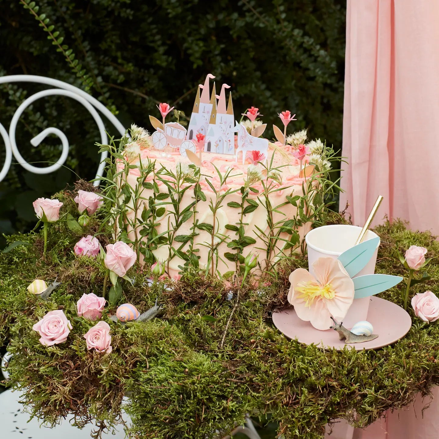Decorative setup with a castle, flowers, and a cup on a moss-covered surface.