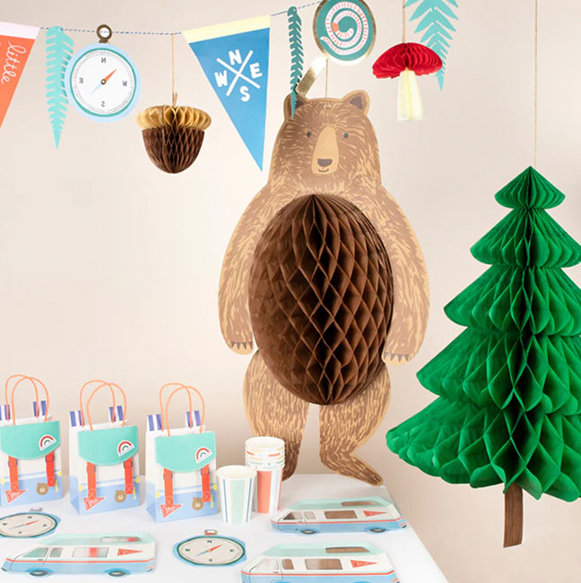 Wooden bear decoration with honeycomb ball, green tree, and party supplies on a table.