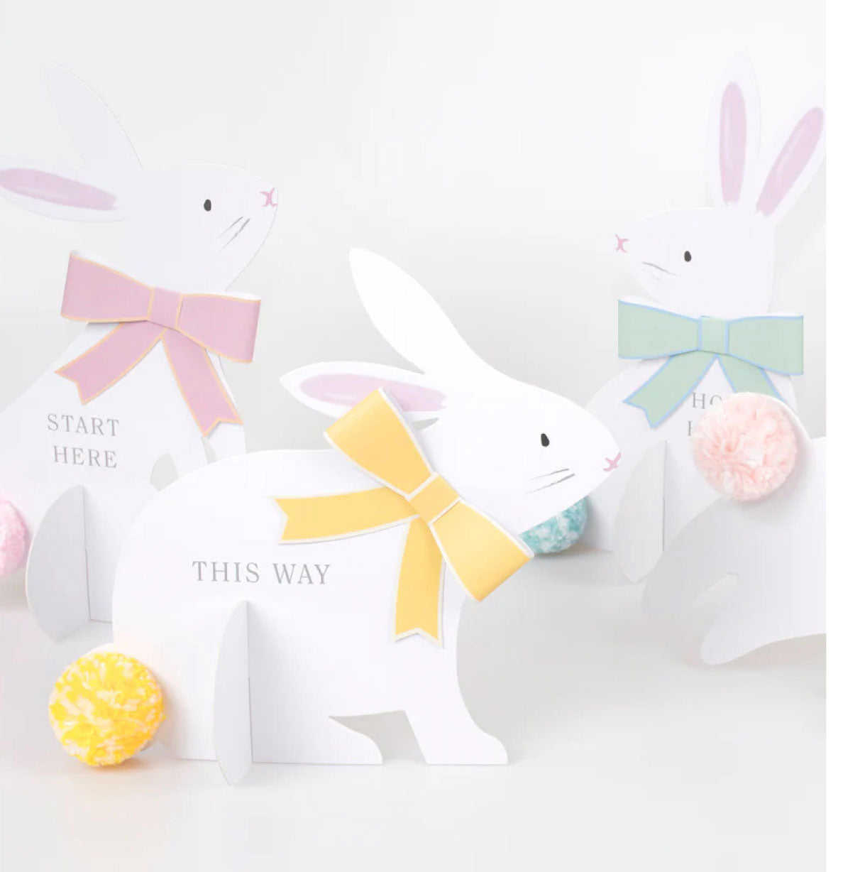 White paper bunny with colorful bow and text on a light gray background